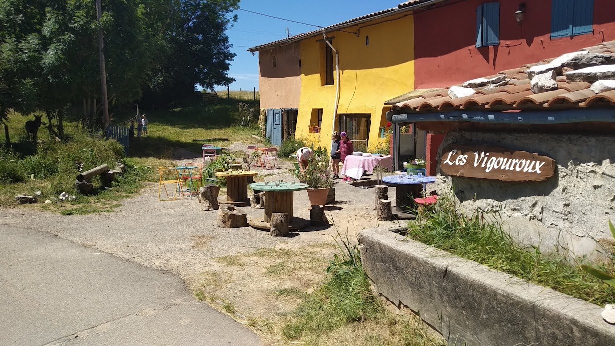 La cour du gîte et ses tables en été, devant la façade jaune et rouge du hameau des Vigouroux