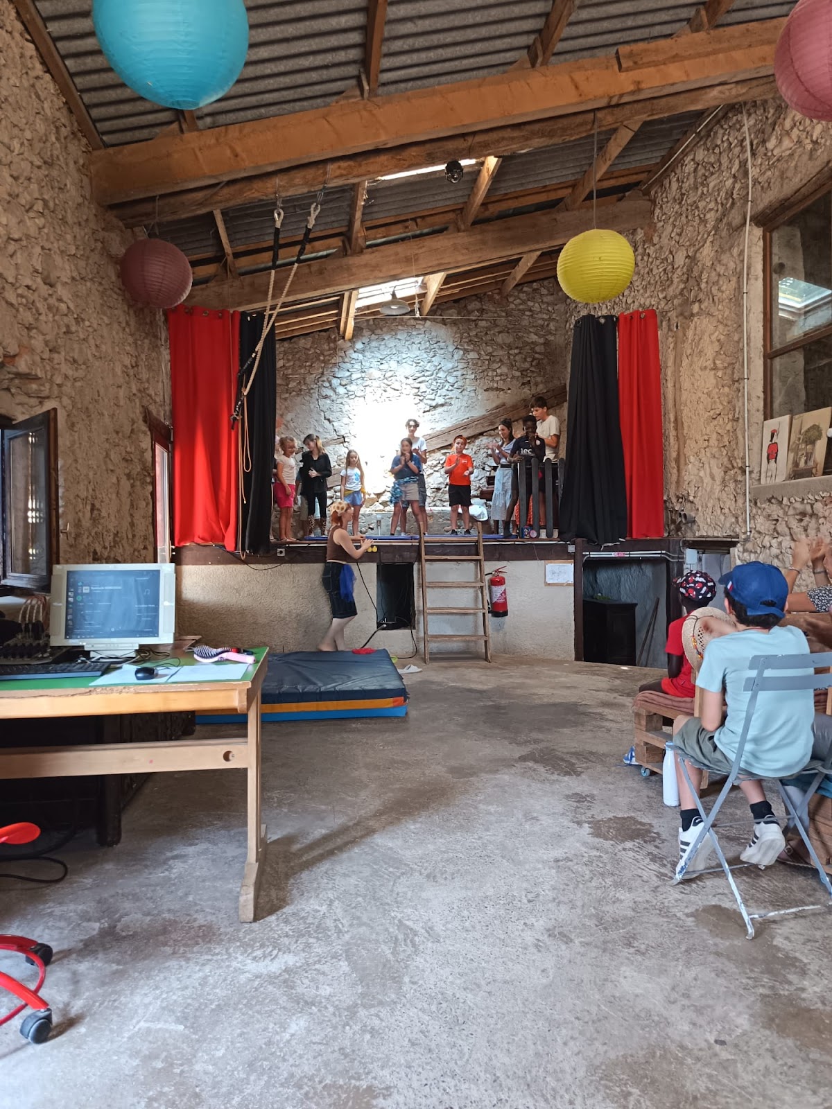 Les enfants alignés sur la scène de la salle des Vigouroux pour le spectacle, sous les lampions et les rideaux rouges