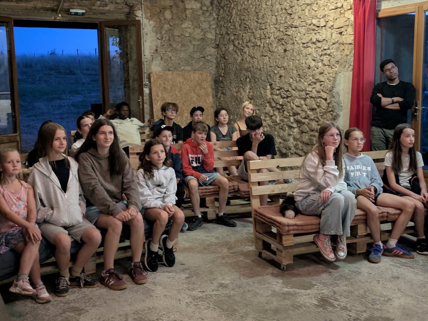 Veillée dans la salle en pierre, enfants assis sur des bancs en palettes