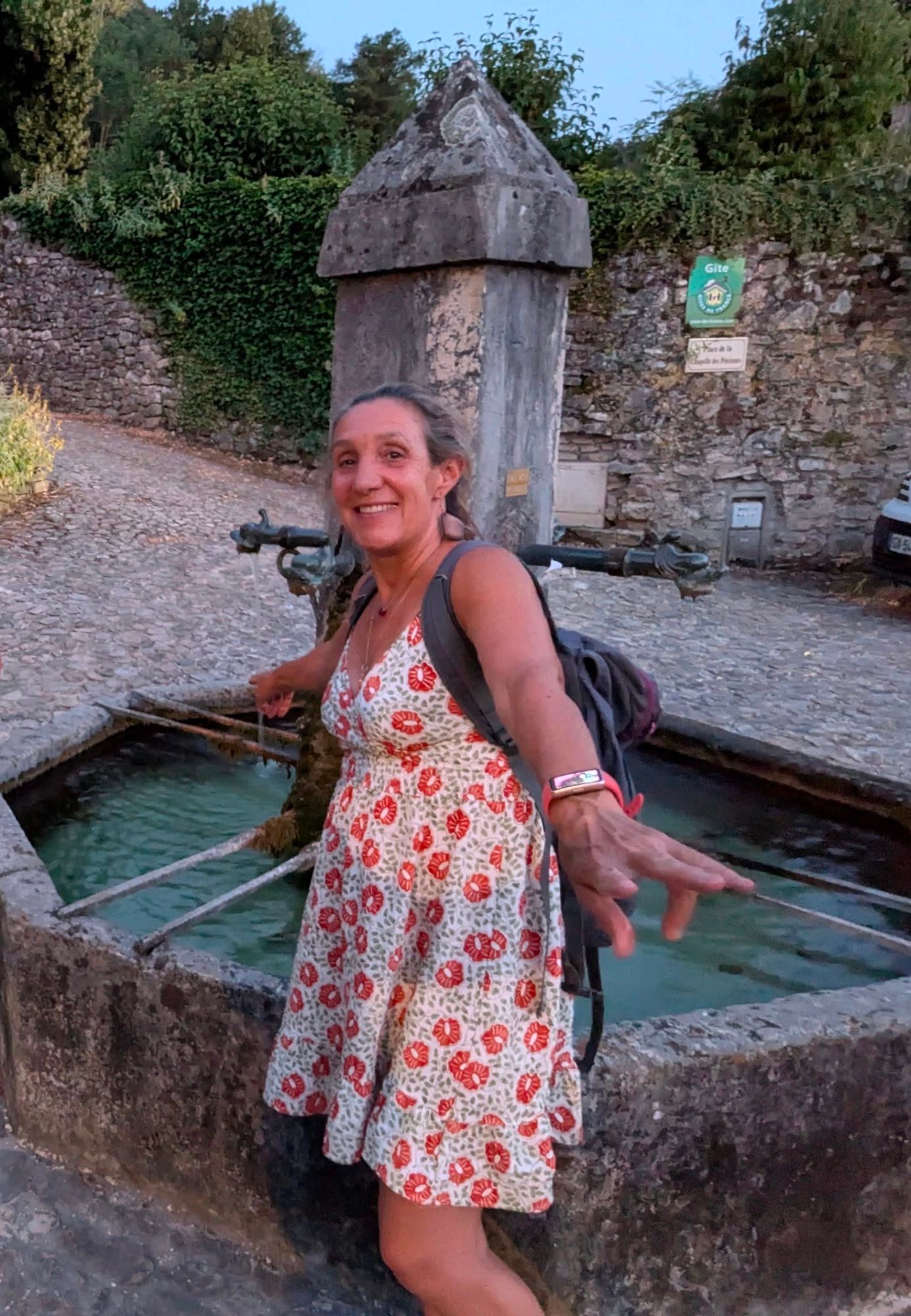 Valérie souriante devant une fontaine du village